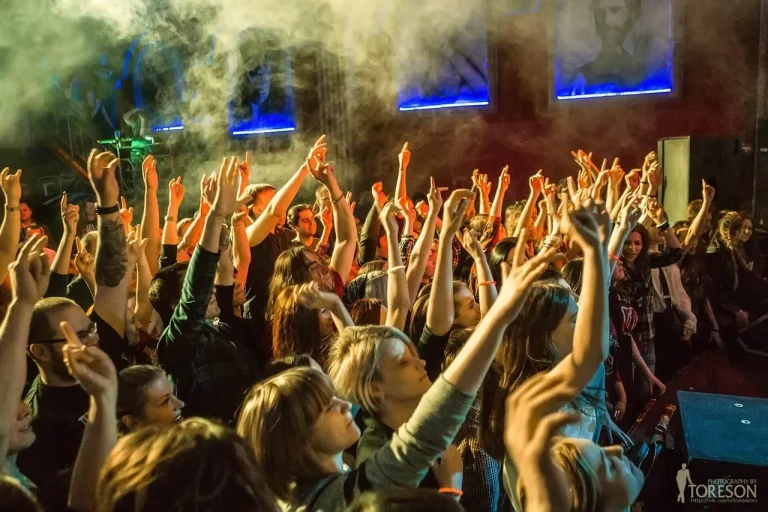 The audience reaches towards the stage in smoke and yellow light