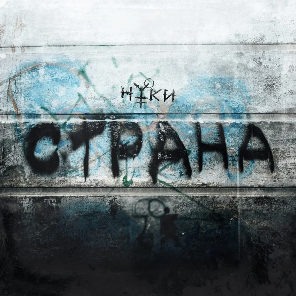 The word “Strana” sprayed in black on a concrete wall with graffiti, the Nuki logo above it
